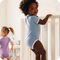 2 toddlers playing in playroom with crib while wearing short sleeve bodysuit in cornflower blue and violet