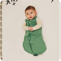 baby lies on their back in green sleeping bag with their hands clasped