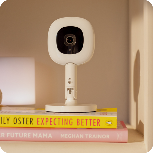 Nanit Pro Baby Monitor + Flex Stand standing on two books in bookshelf