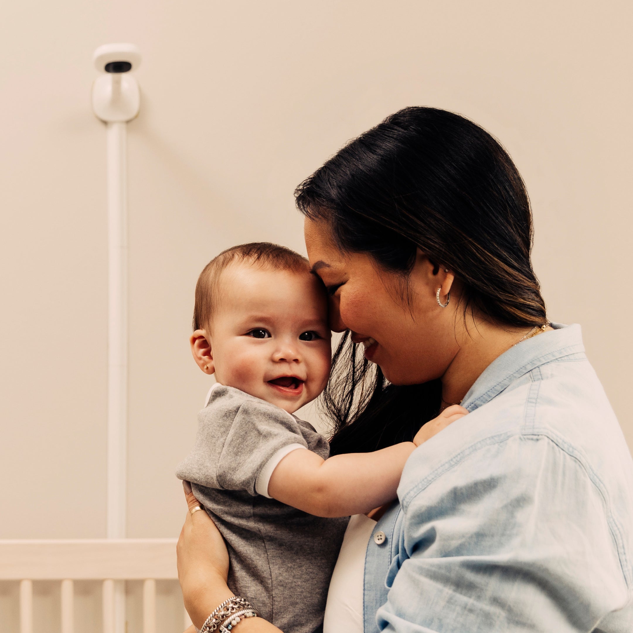 mom holding baby with nanit pro monitor and wall mount in the background over a crib