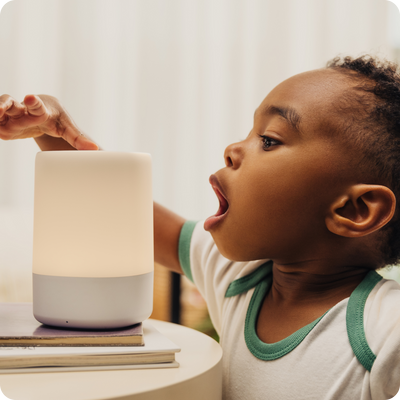 toddler wearing nanit sleep wear short sleeve bodysuit in spruce green reaching out to use the nanit sound and light