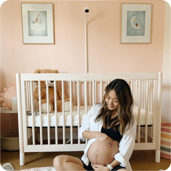 Pregnant woman in a nursery with a crib and teddy bear and Pro Baby Monitor + Wall Mount