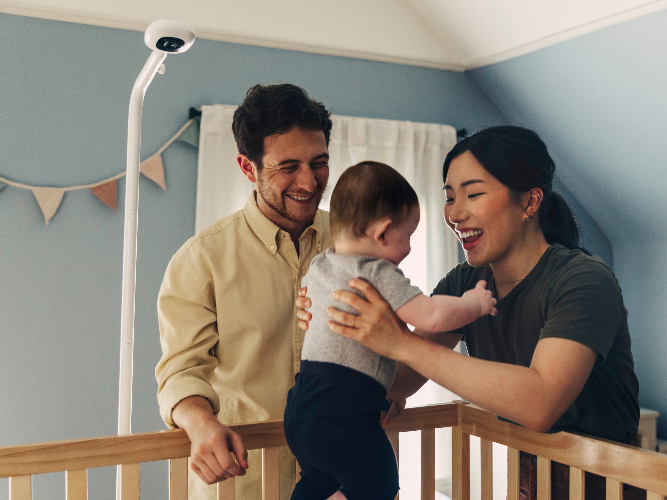 Family in a nursery with a baby standing on a crib, smiling.