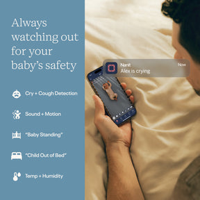 Person holding a smartphone with app notifications on a bed, emphasizing baby safety monitoring features.