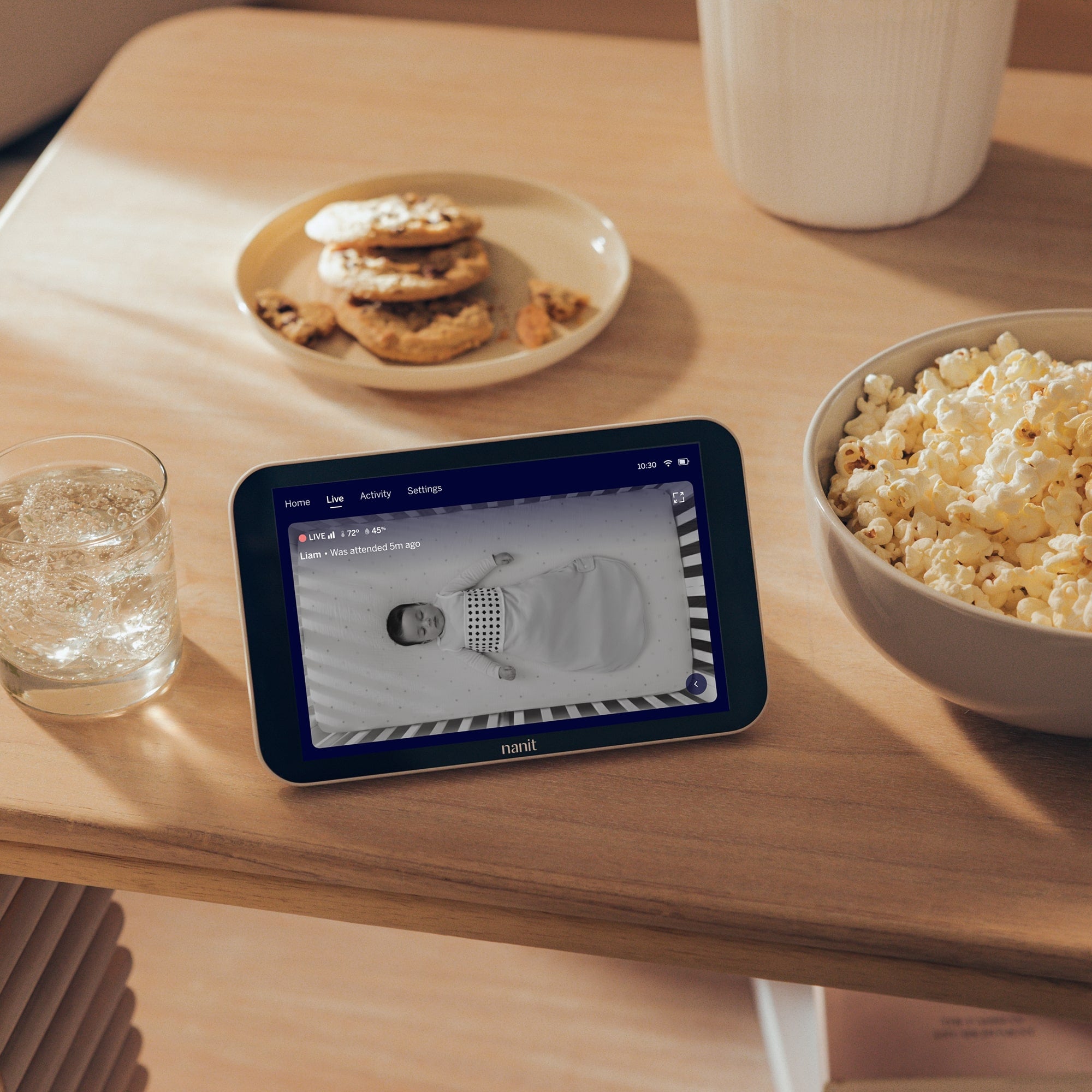 Nanit Home on a table with cookies, popcorn, and water.