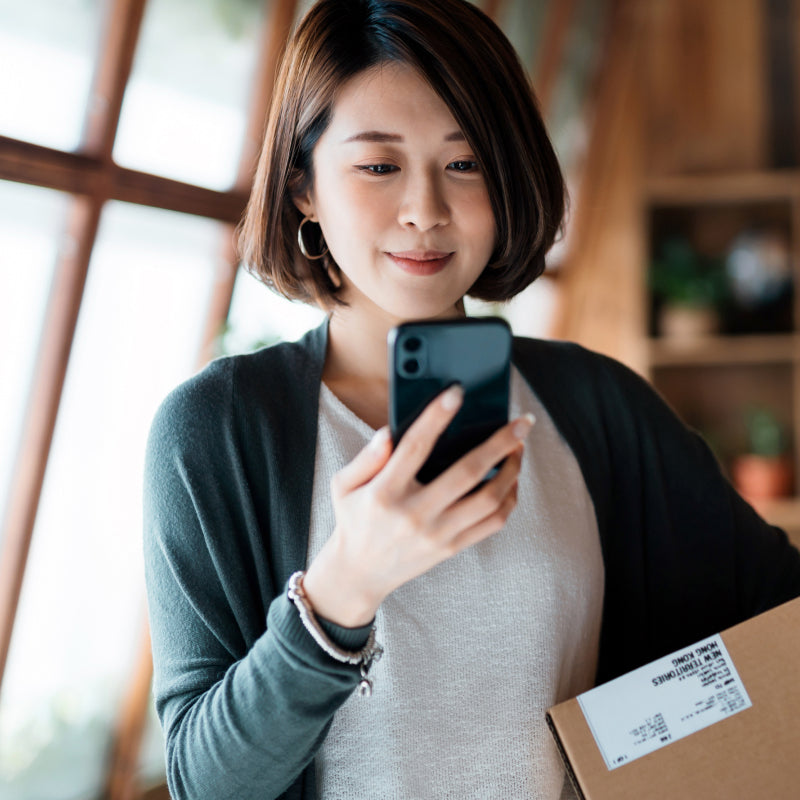 woman looking at mobile with shipping box under her arm