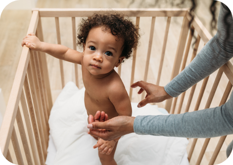 baby in crib with woman reaching out to him 