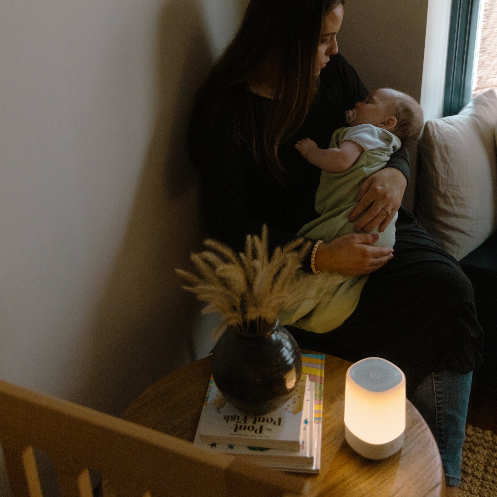 mom holding sleeping baby with nanit sound + light on table