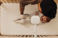 Toddler being out down on crib by man with nanit pro camera with flex stand overhead