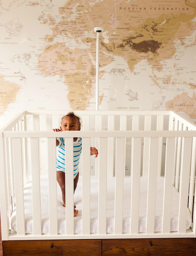 child reaching over to end of crib with nanit floor stand in background
