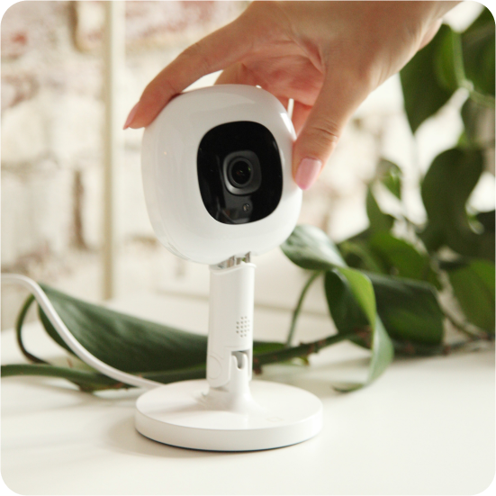 Pro Baby Monitor on Flex Stand with a hand reaching towards it, set against a blurred indoor background with greenery.