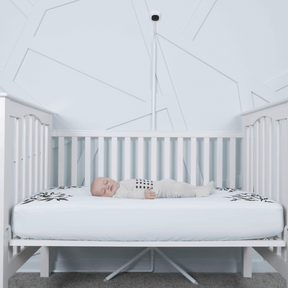 baby sleeping in nanit pajamas in crib covered in blue smart sheet with nanit pro and clearance floor stand in front of crib #color_blue
