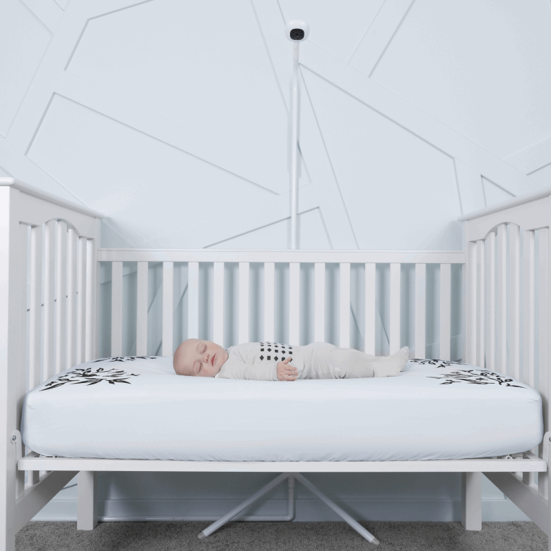 baby sleeping in nanit pajamas in crib covered in blue smart sheet with nanit pro and clearance floor stand in front of crib #color_blue