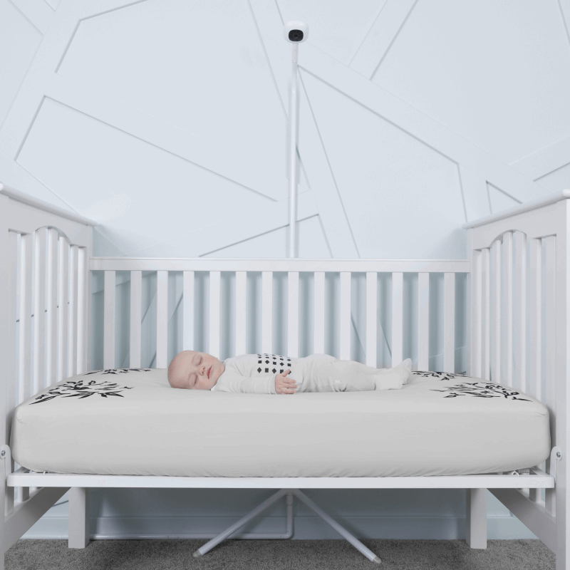 baby sleeping in nanit pajamas in crib covered in gray smart sheet with nanit pro and clearance floor stand in front of crib #color_gray