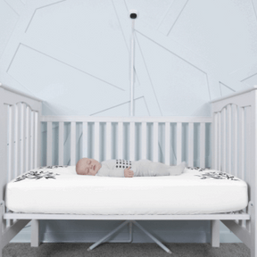 baby sleeping in nanit pajamas in crib covered in white smart sheet with nanit pro and clearance floor stand in front of crib #color_white