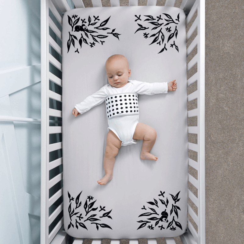 baby wearing breathing band laying on crib with gray smart sheet covered #color_gray
