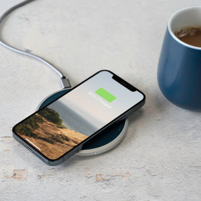 iphone charging on dual-purpose charging pad with coffee mug on the right