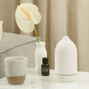 Vitruvi Stone Ceramic Diffuser on top of book with Vitruvi Sleep Essential Oil Blend