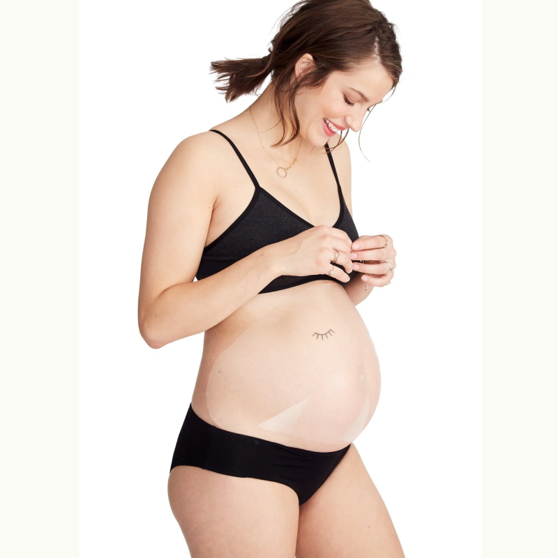 Pregnant woman smiling showing sheet mask on belly