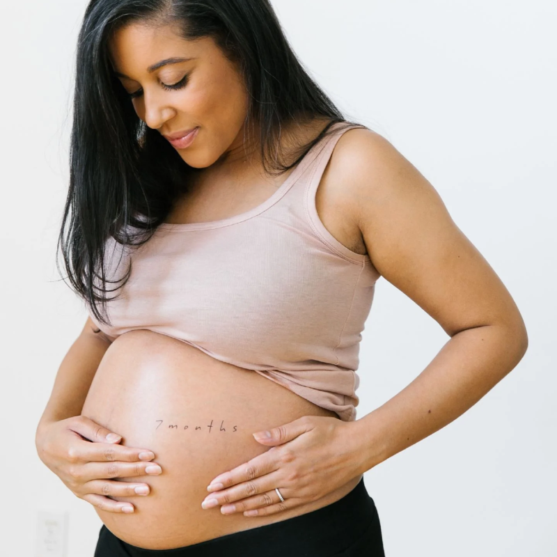 pregnant woman placing hand on belly and shows 7 months belly tattoo on belly