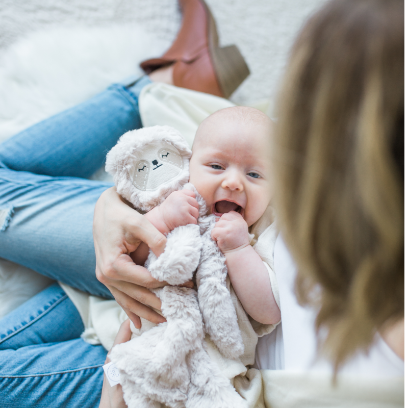 Baby holding Sloth Snuggler while mom holds baby